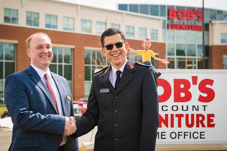 A Bob's store manager and a representative from the Salvation Army shake hands.